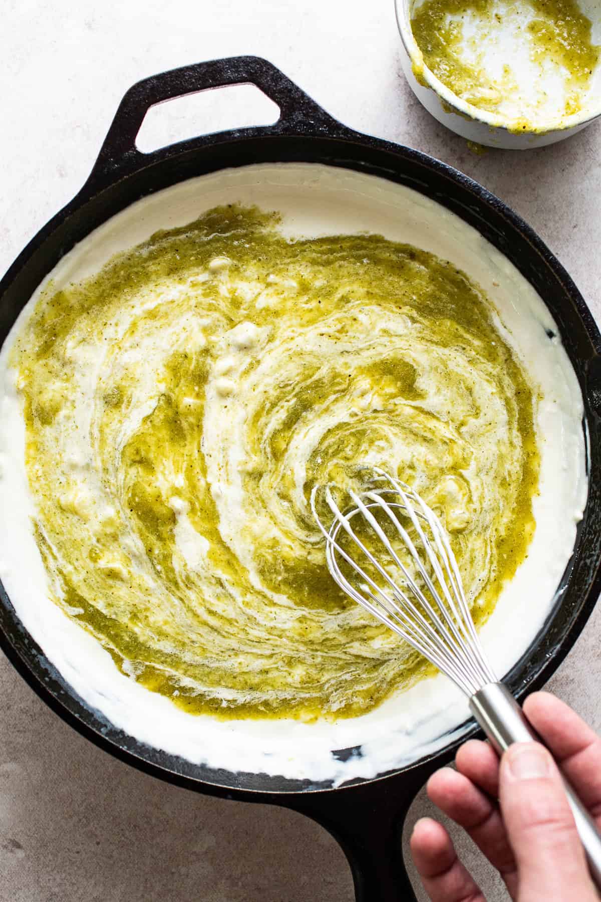 Salsa verde, onions, garlic, butter, milk, and cream cheese in a skillet being melted together and whisked.