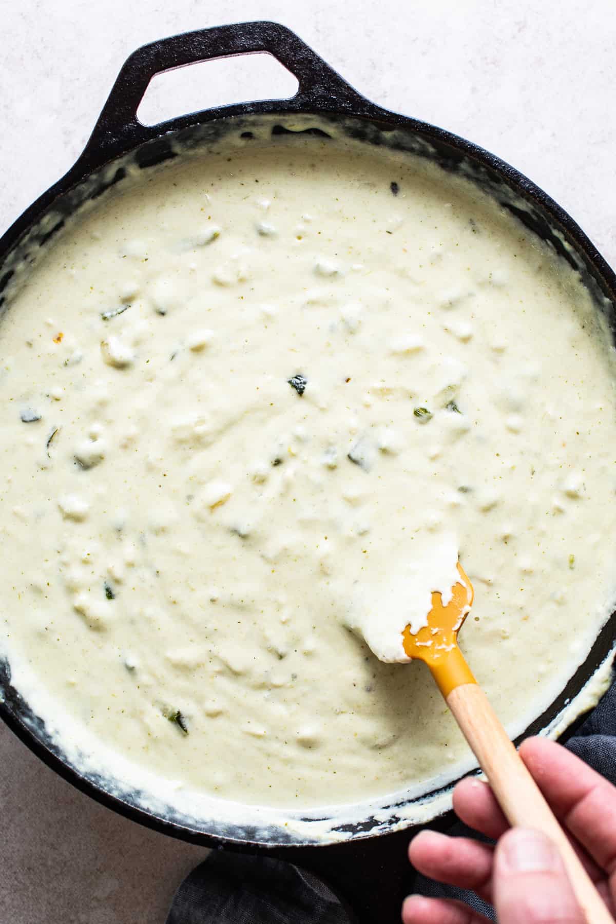 Melted shredded cheese being mixed into a large skillet to make salsa verde queso.