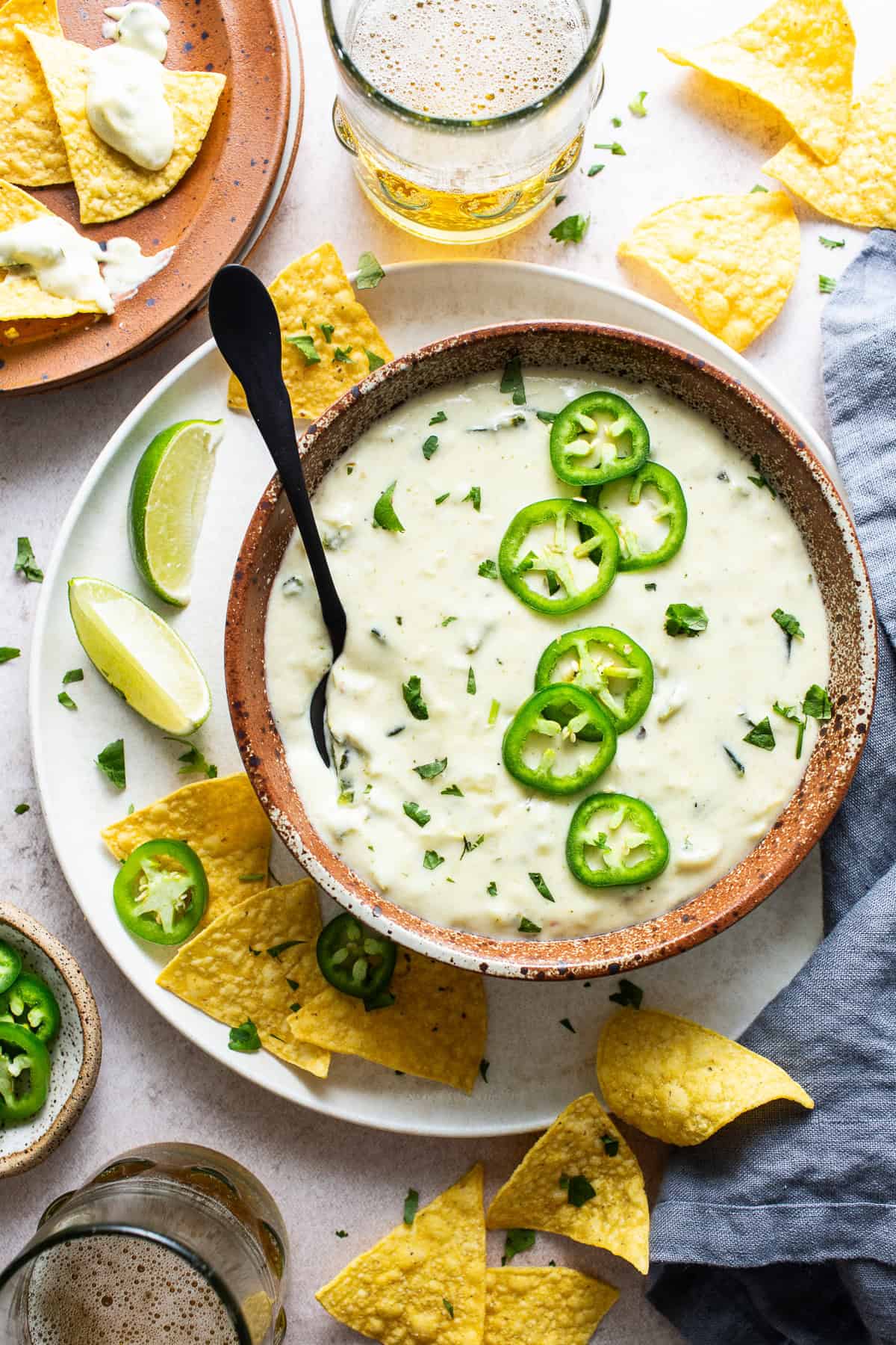 A bowl with salsa verde queso dip topped with jalapeño slices and sided with chips. 