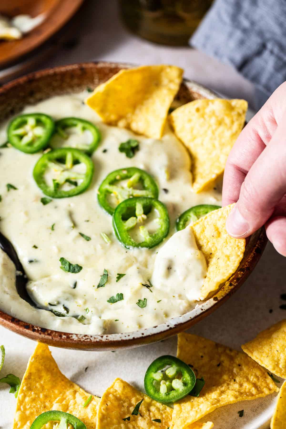 A tortilla chip being dipped into a bowl of salsa verde queso.