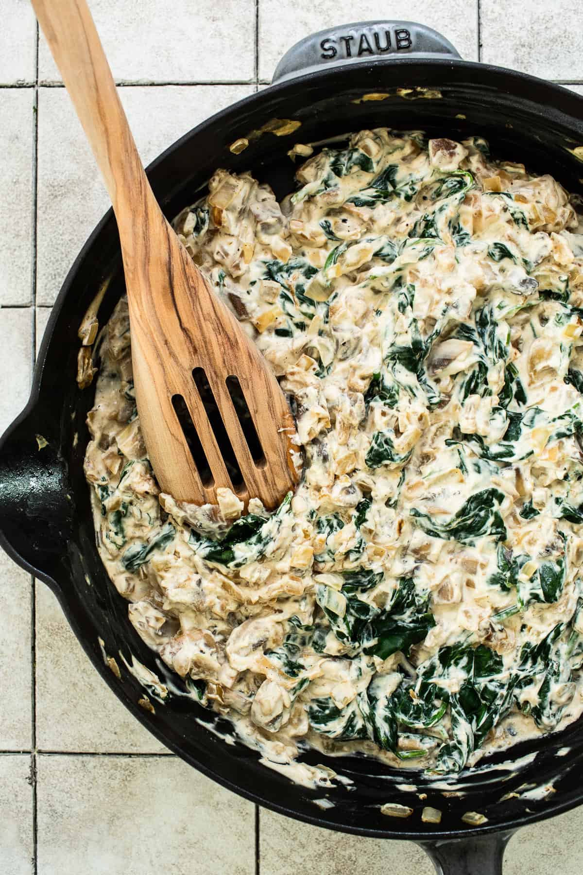 A skillet with the filling ingredients for spinach enchiladas sautéed with seasonings. 