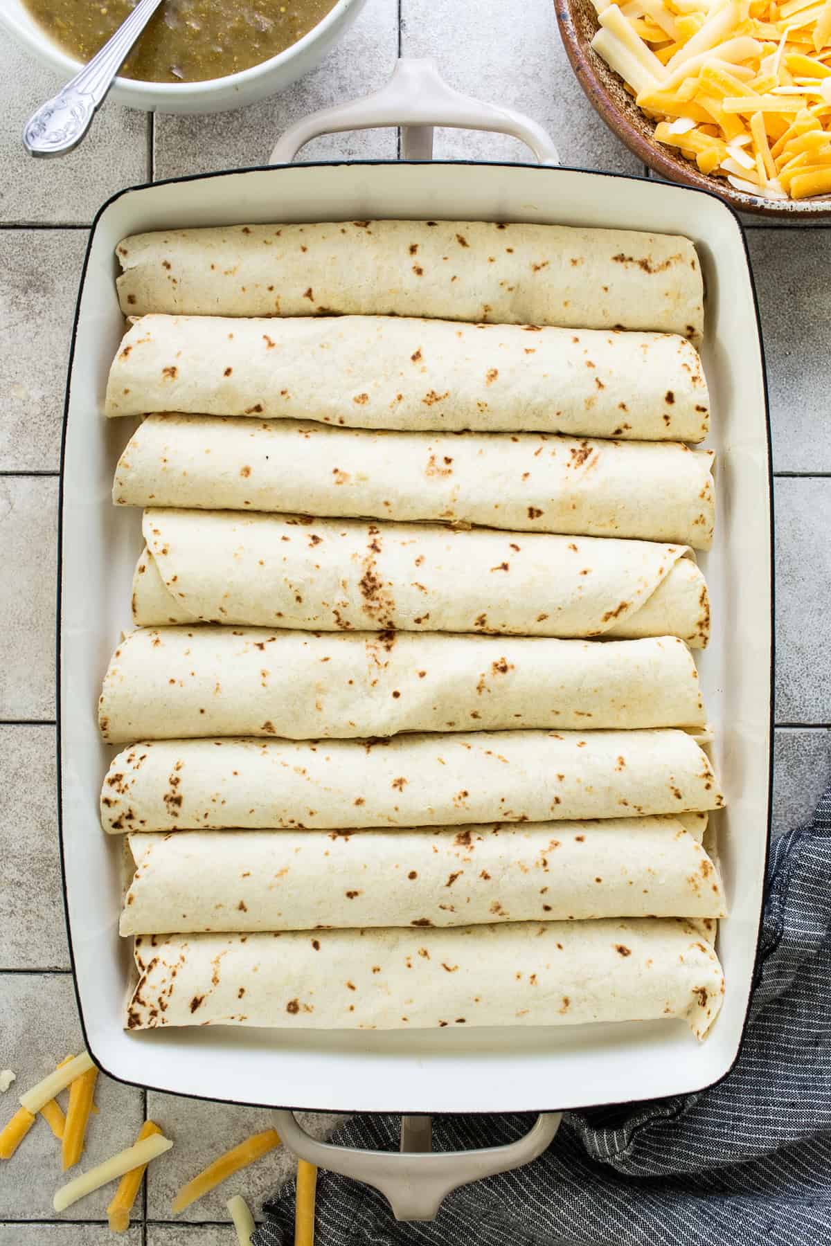 Flour tortillas rolled up with spinach enchilada filling inside a baking sheet.