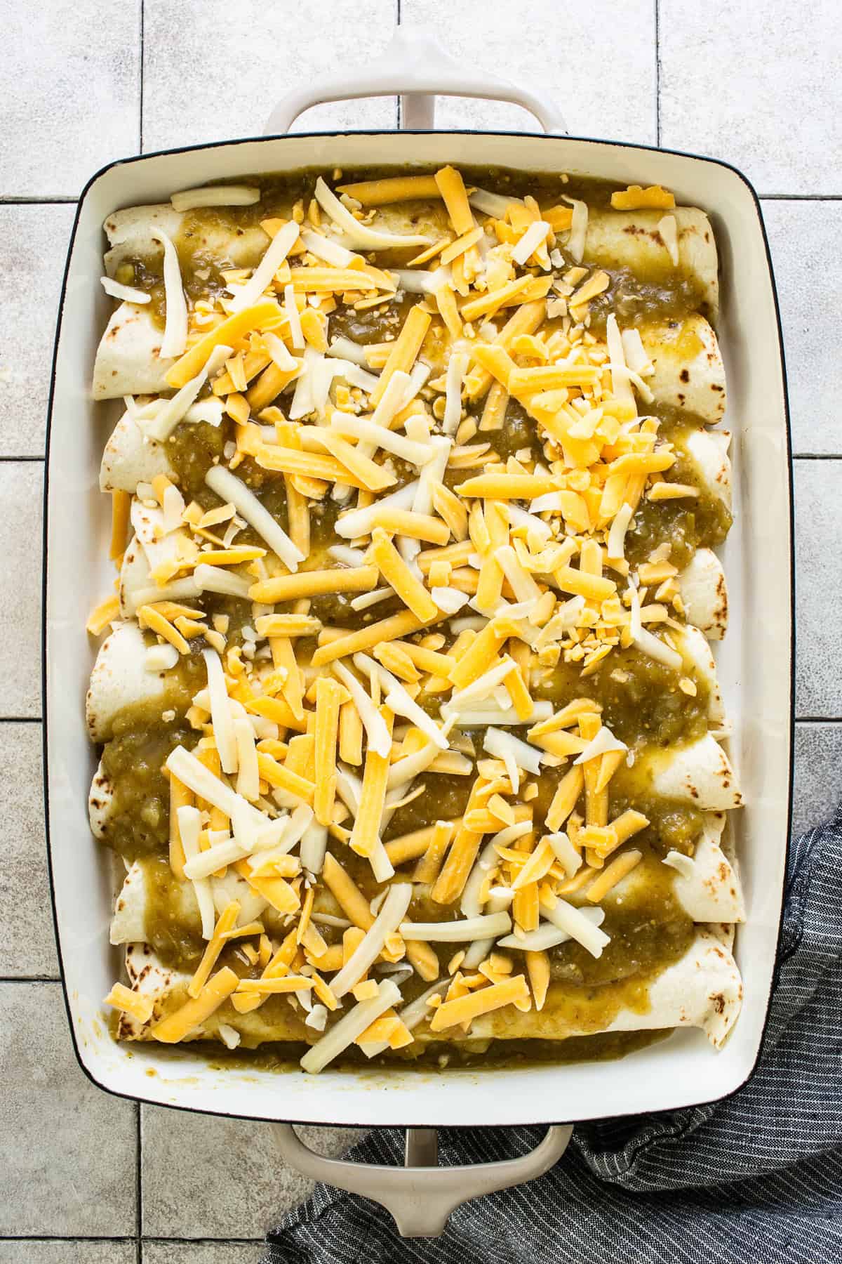 Green salsa and shredded cheese spread over the top of the assembled enchiladas. 