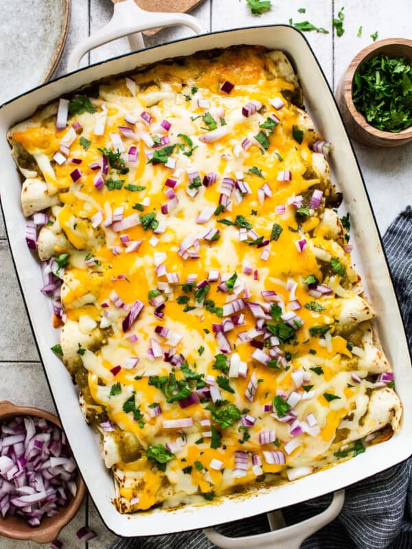 Spinach enchiladas in a baking dish topped with melted cheese, salsa verde, onions, cilantro, and sour cream or Mexican crema.