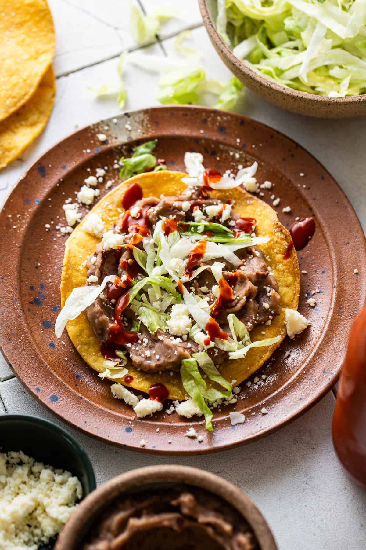 A tostada shell with refried beans, lettuce, cheese, and salsa on top. 