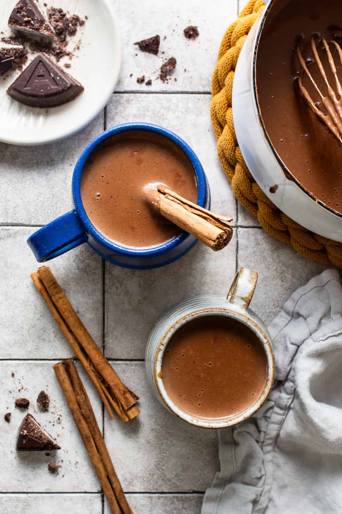 The saucepan filled with champurrado is being served into two separate mugs ready to enjoy.