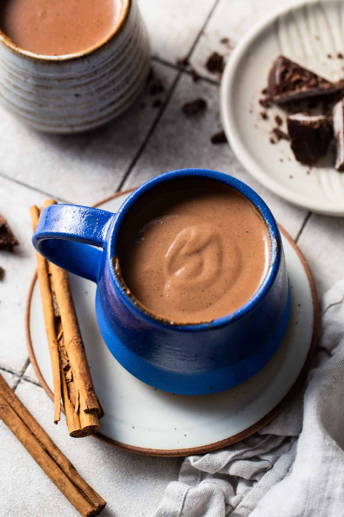 A serving of champurrado in a mug with cinnamon sticks on the side.