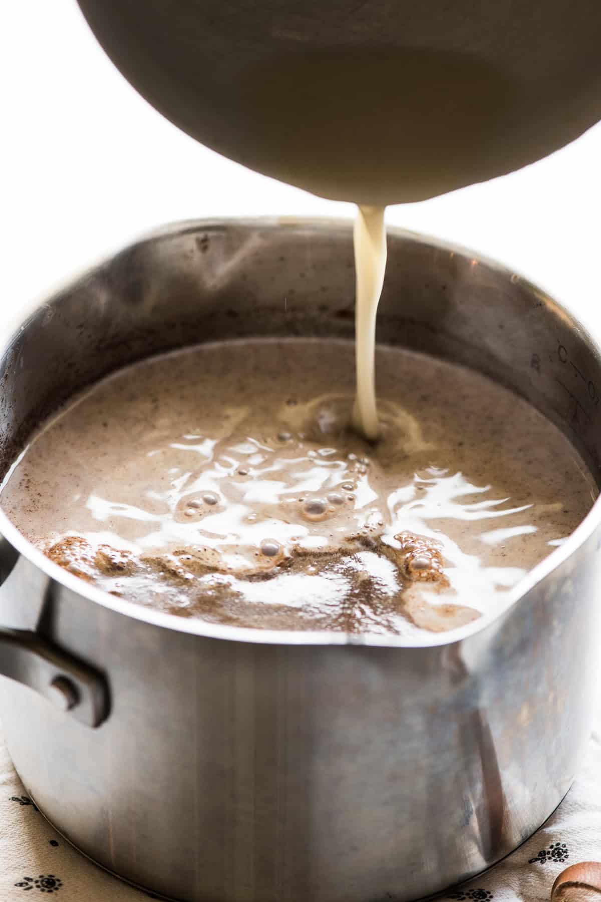 The masa harina mixture being poured into the saucepan of the chocolate mixture.