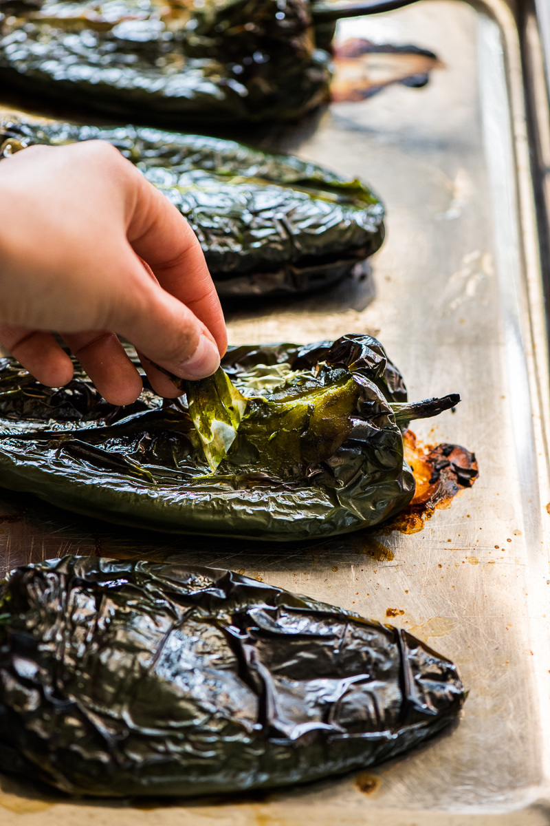 Roasted poblano peppers laid out on a baking sheet while the skin is being peeled.