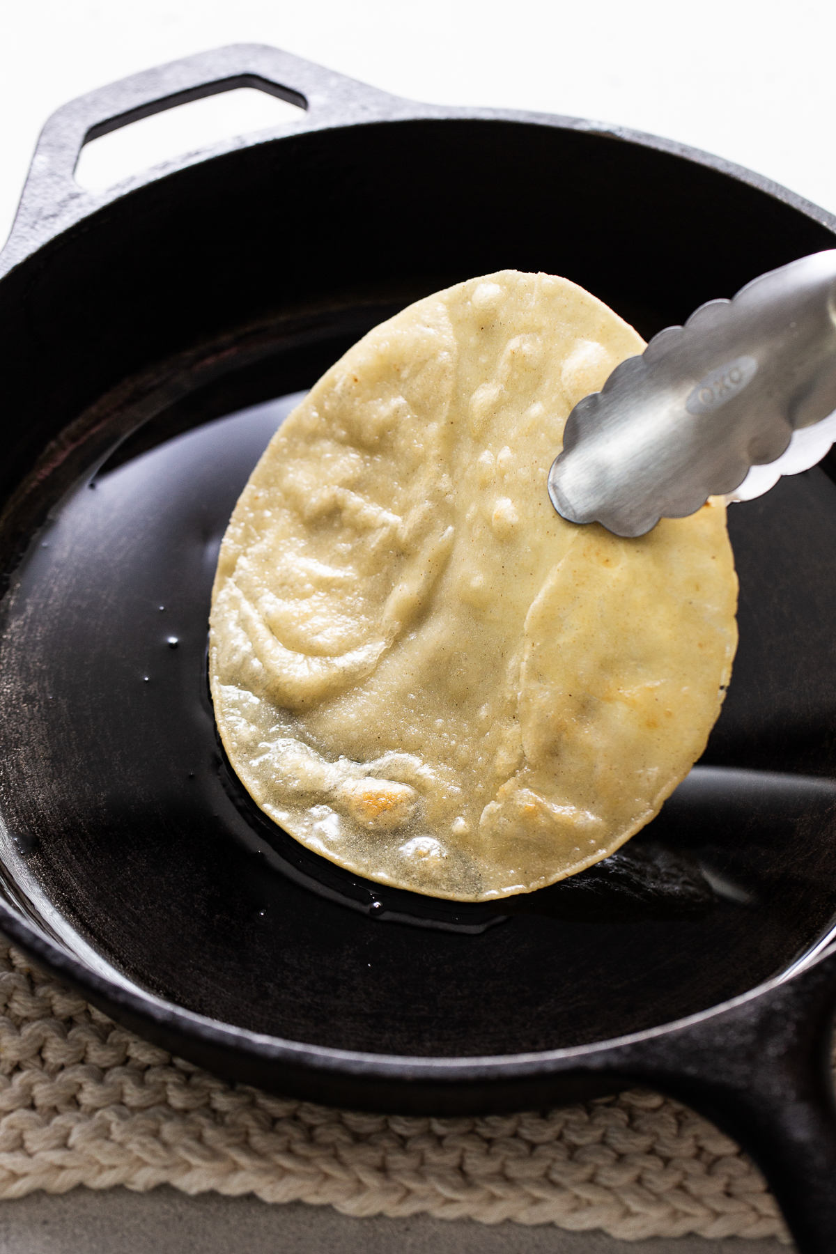 A corn tortilla being fried in a skillet with oil.