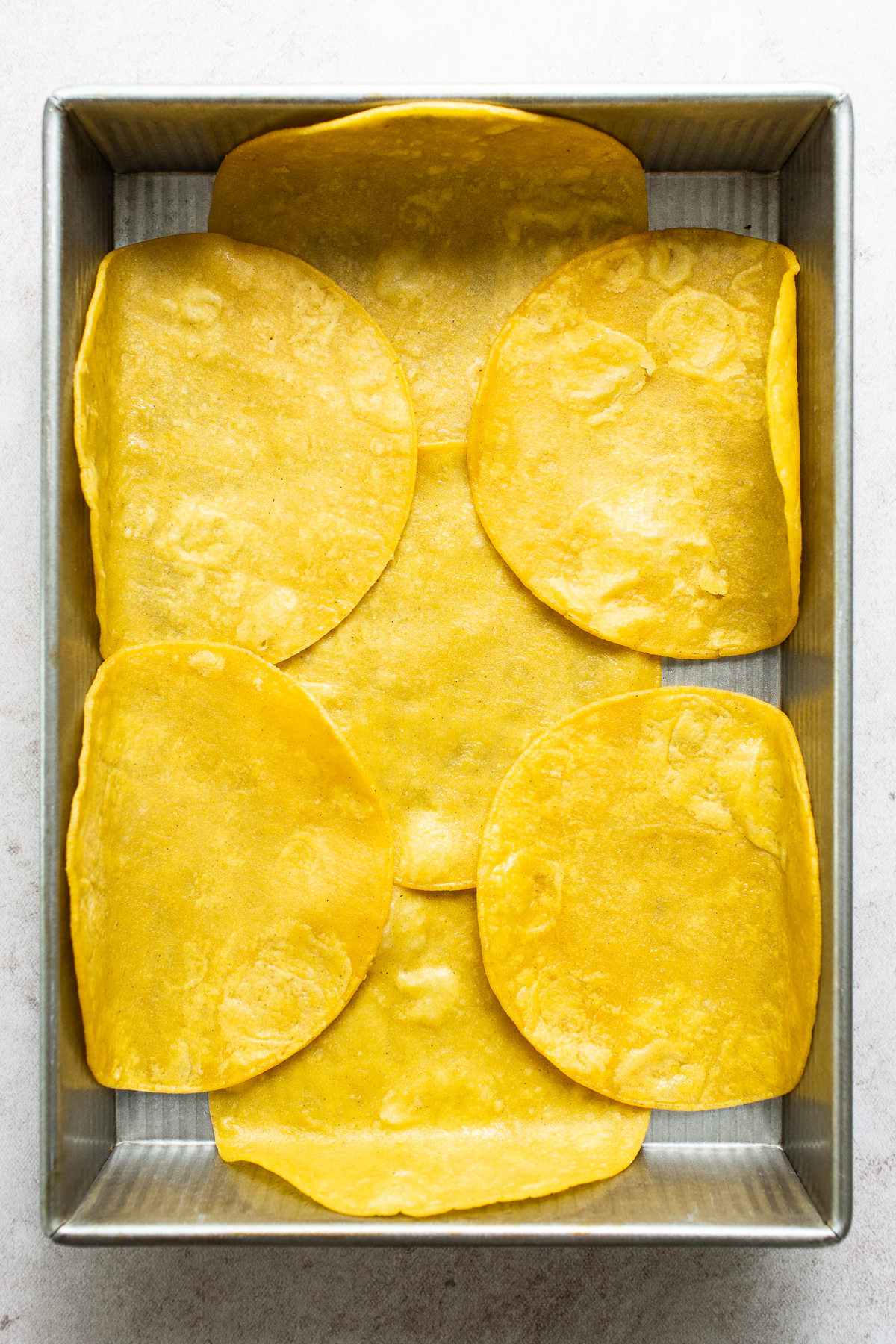 A layer of lightly fried corn tortillas on the bottom of a baking dish.