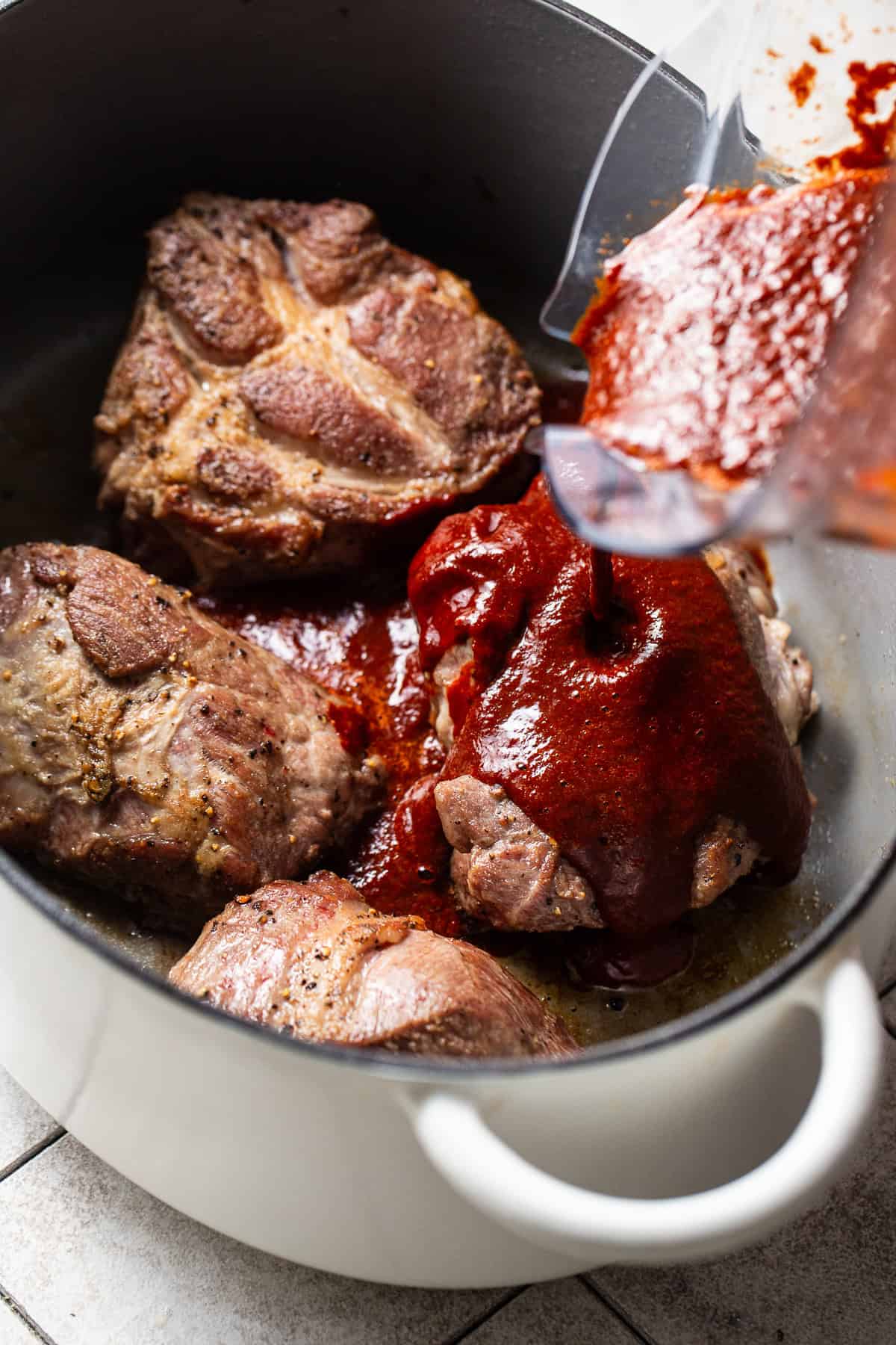 The chile broth being poured into the pot with the seared meat to make pozole rojo.