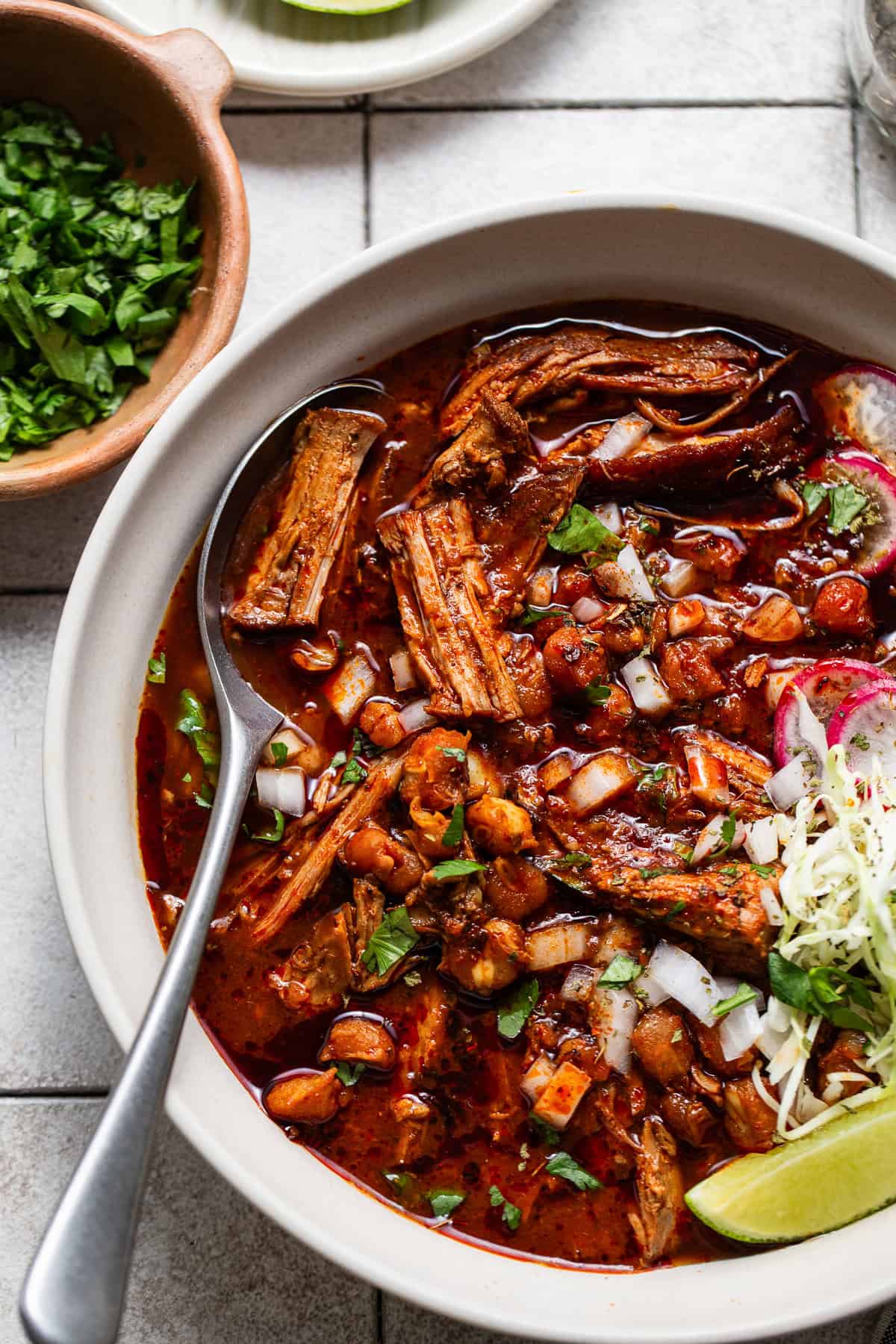 Delicious pozole rojo served into a bowl topped with cabbage, radishes, limes, and onions.