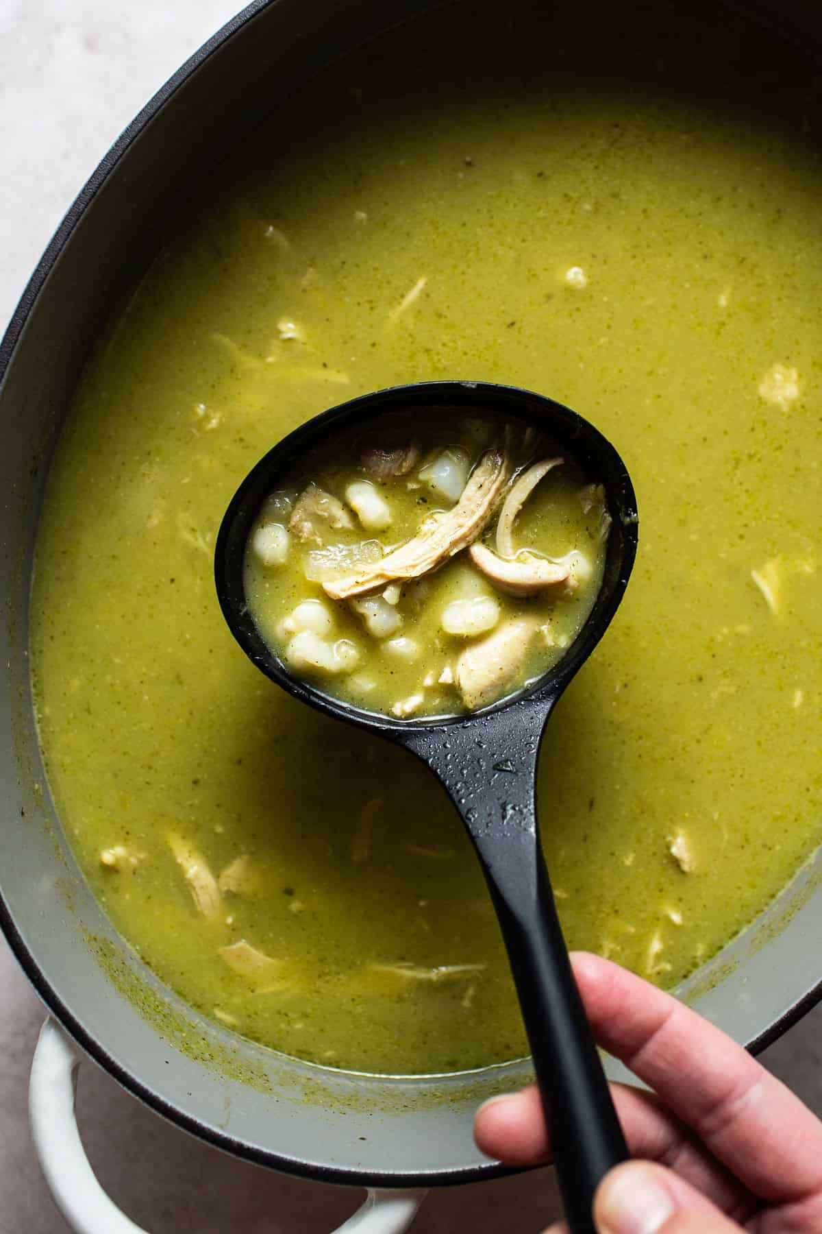 Cooked pozole verde in a large pot with a ladle spooning out some of the soup.