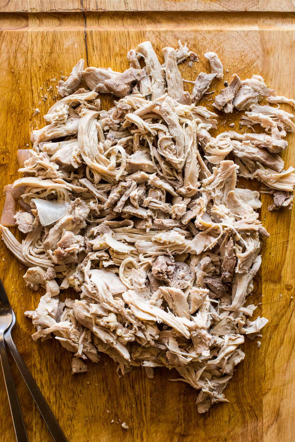 A cutting board with cooked shredded chicken for chicken pozole verde.