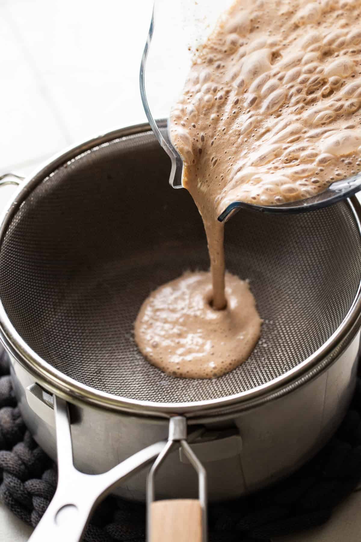 Atole de nuez being poured through a fine mesh strainer into a pot.