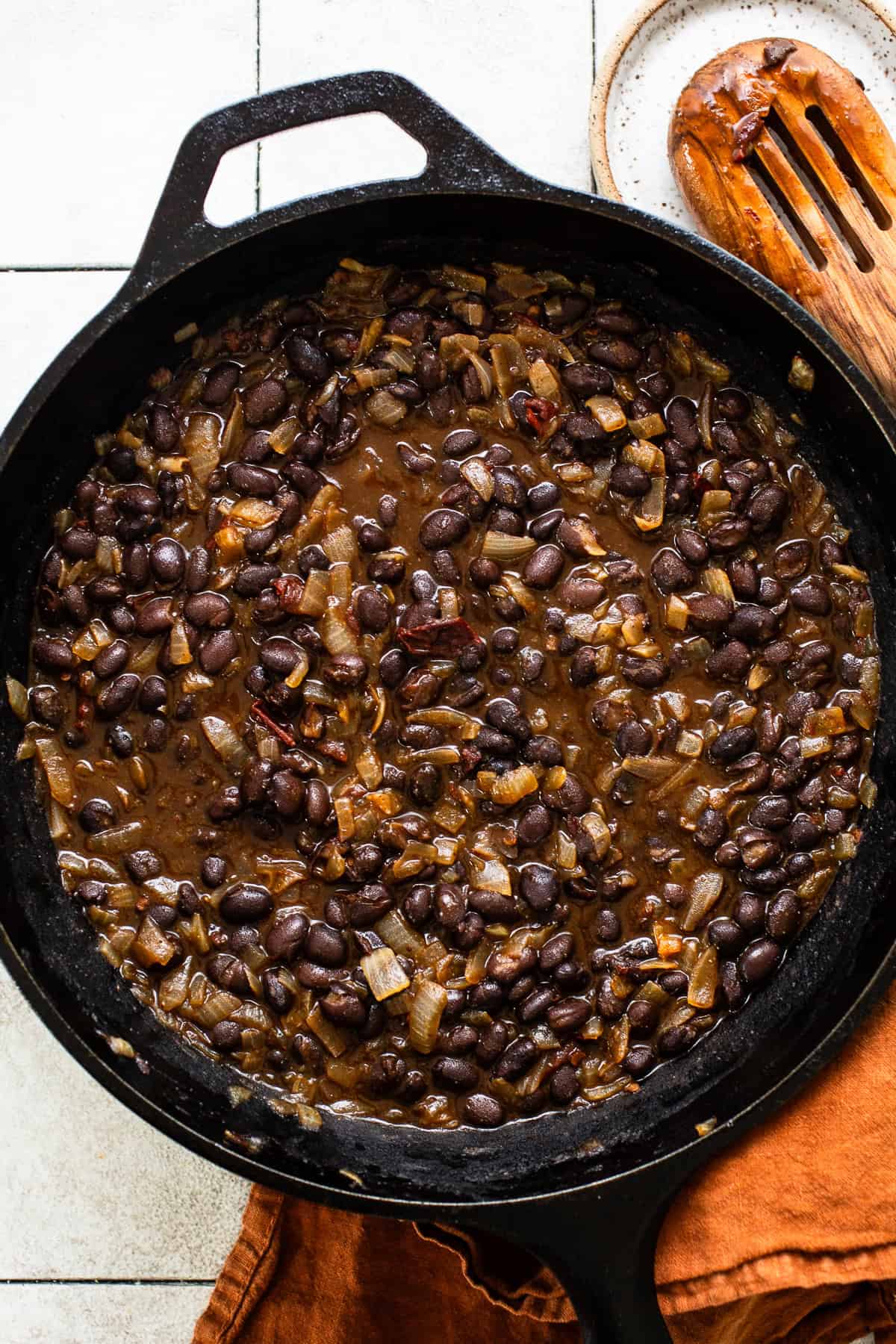 A mixture of cooked black beans with onions and chipotle peppers in adobo sauce in a cast iron skillet to make black bean tostadas.