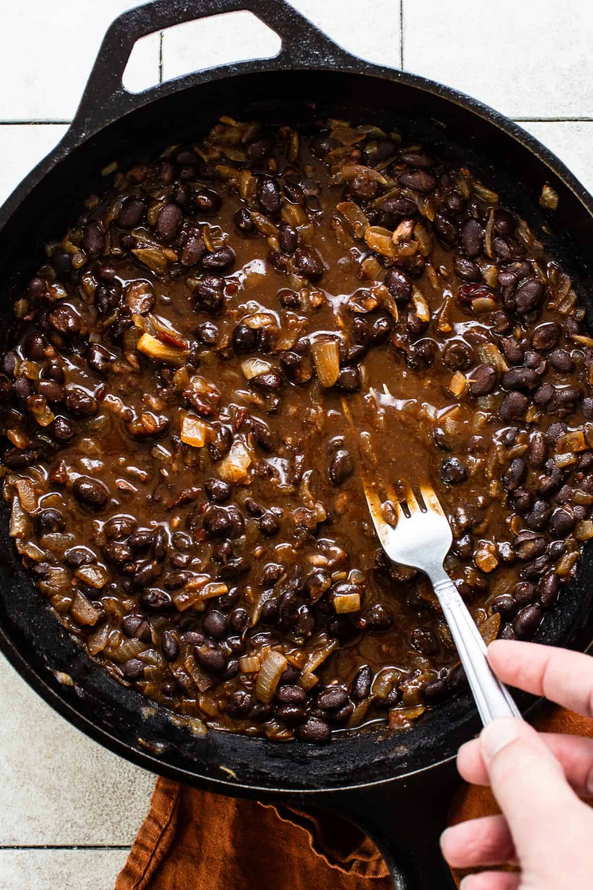 A fork mashing a skillet of black beans.