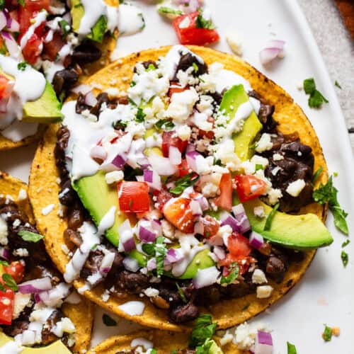 Black bean tostadas topped with avocado, cilantro, tomatoes, and sour cream.