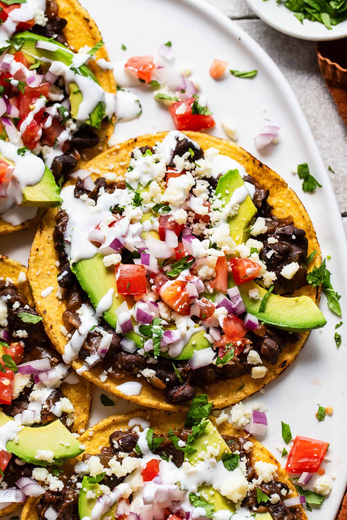 Black bean tostadas topped with avocado, cilantro, tomatoes, and sour cream.