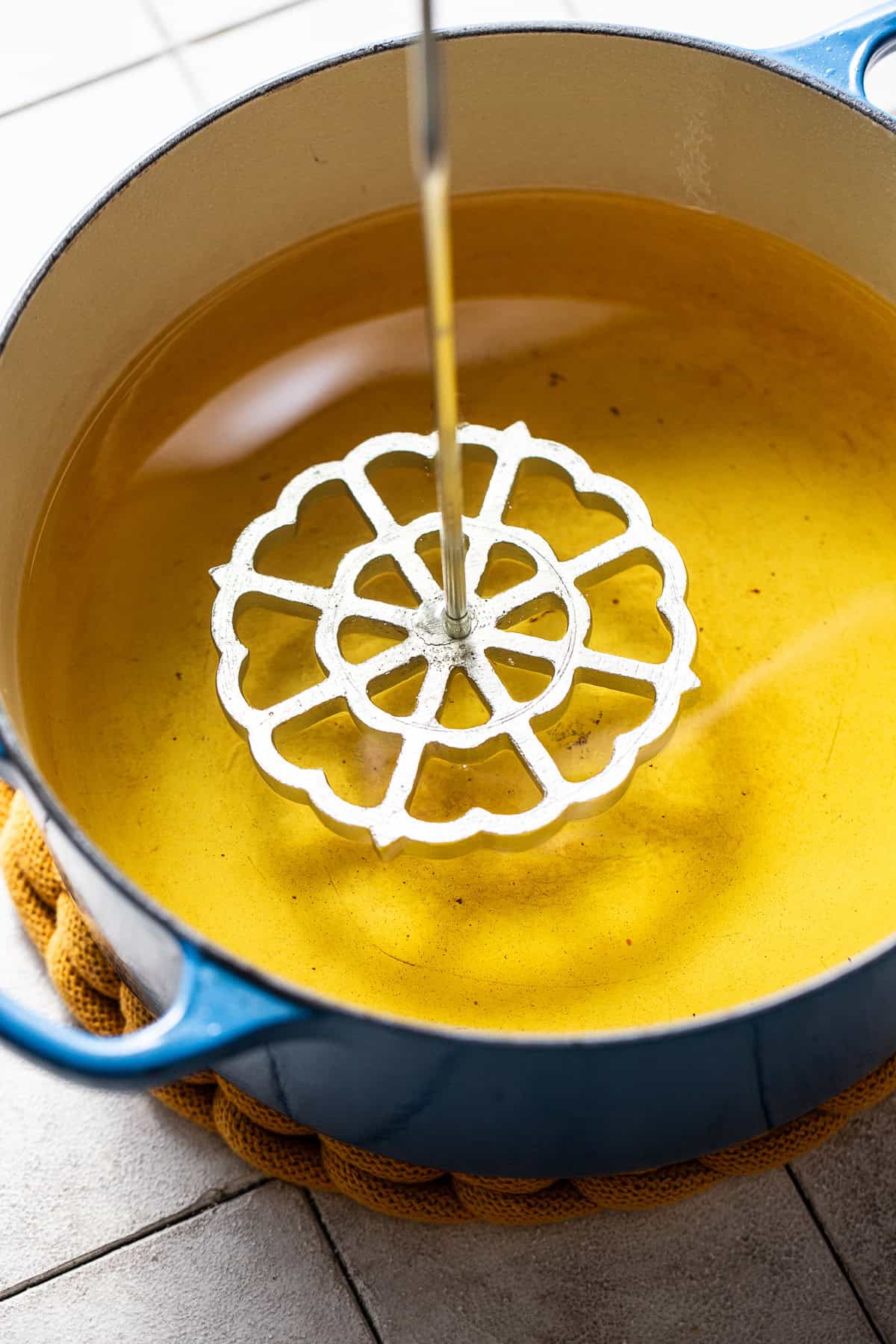 A metal mold for a buñuelo de viento being dipped in hot boil.