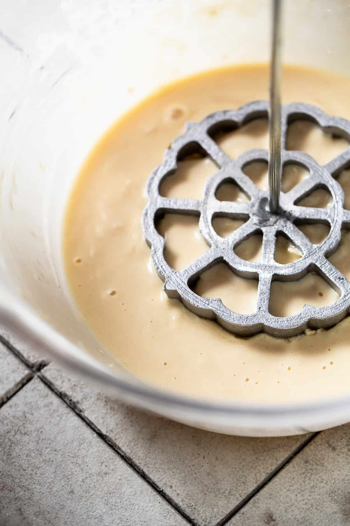 A hot iron mold being dipped into a bowl filled with batter for buñuelos de viento.