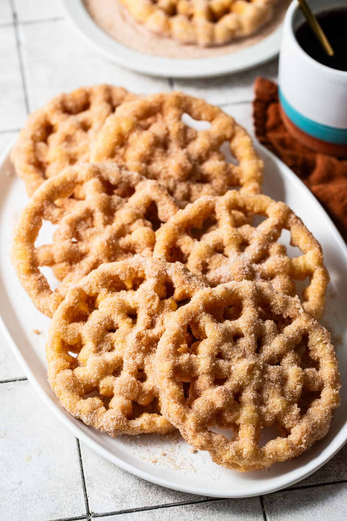 Freshly made buñuelos de viento  served on a large serving tray coated in cinnamon sugar mixture. 