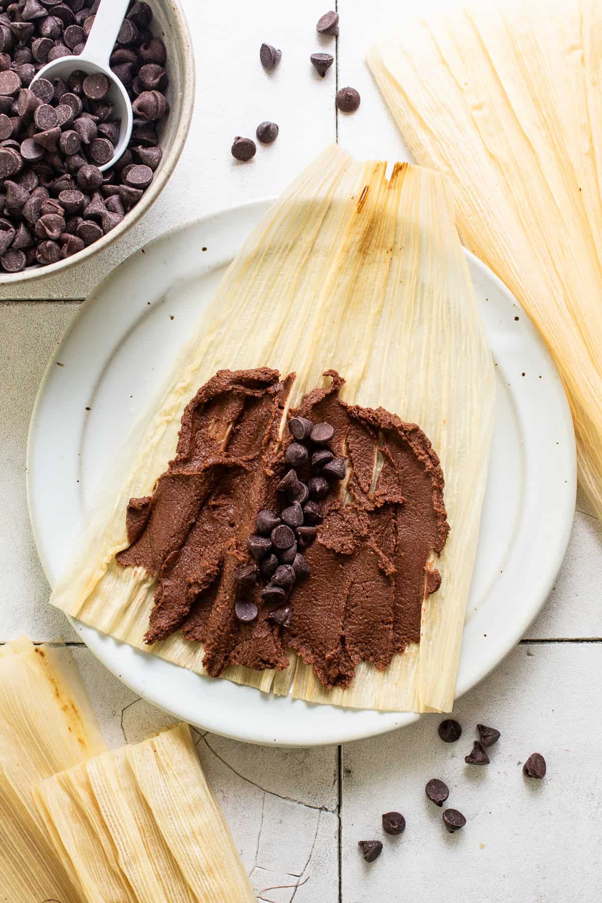 Masa spread on a corn husk with chocolate chips in the middle to make chocolate tamales.