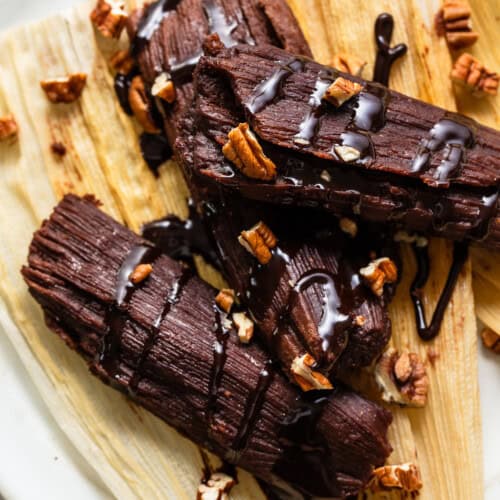 Chocolate tamales drizzled with a chocolate sauce and chopped pecans on a corn husk.