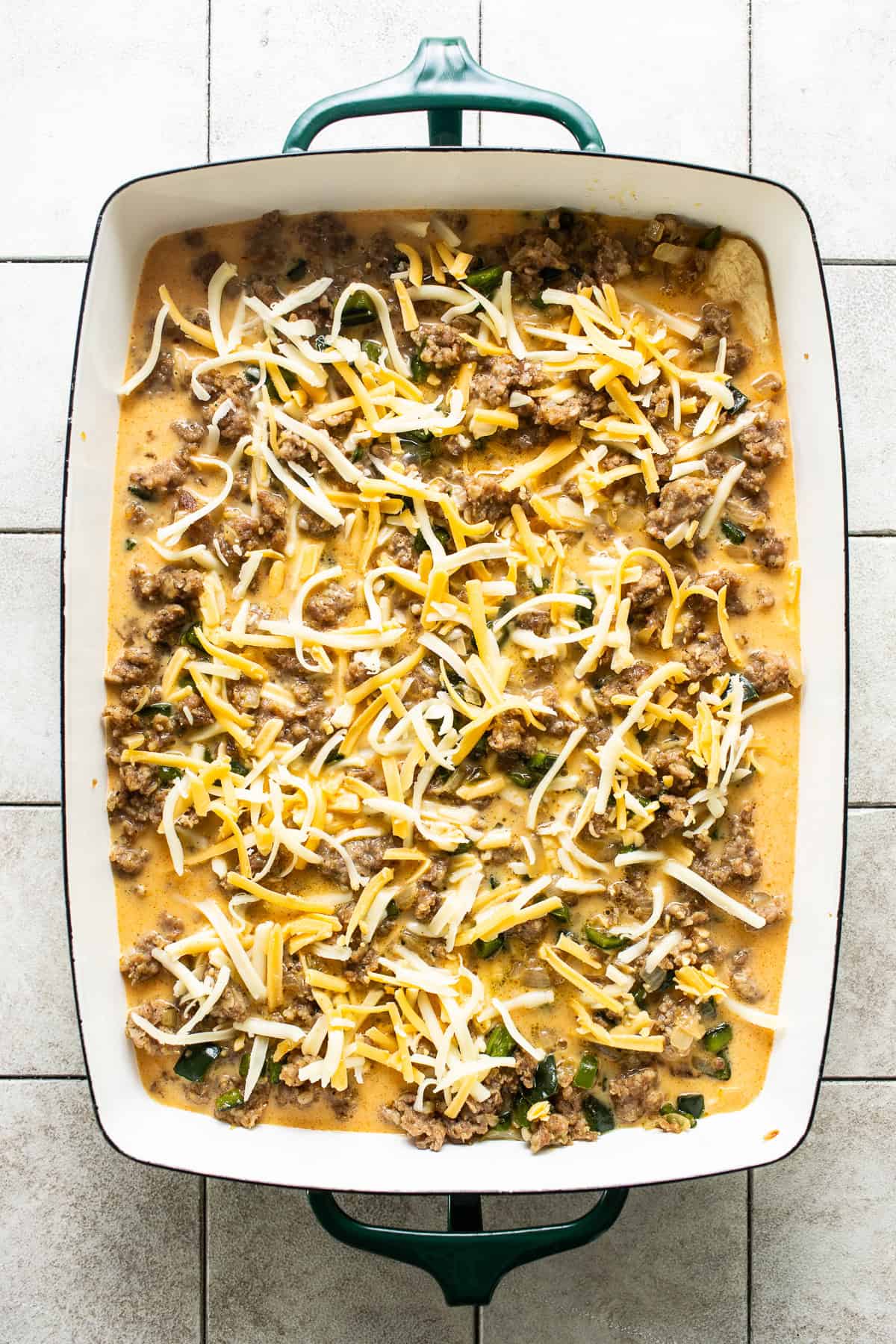 Whisked eggs, cooked breakfast sausage, peppers, onions, and shredded cheese in a baking dish to make crescent roll breakfast casserole.