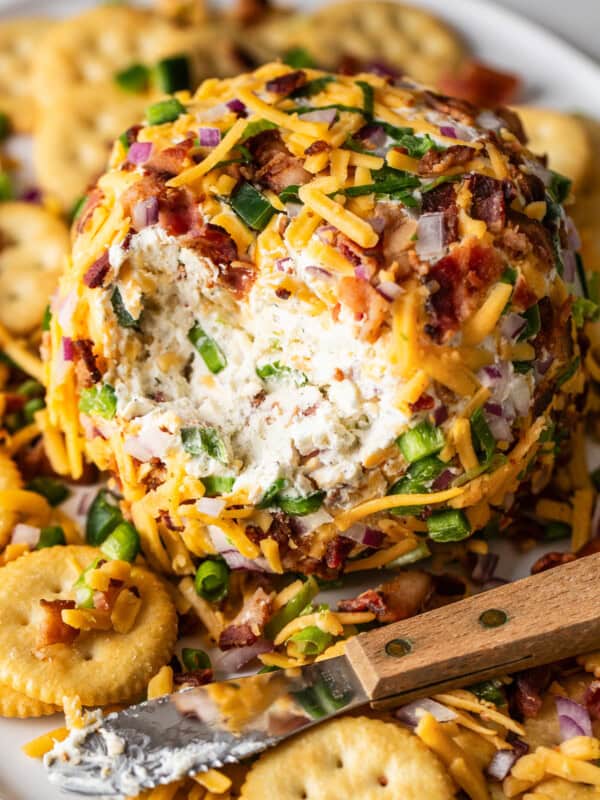 An easy jalapeño cheese ball covered with bacon and cheddar on a plate with crackers.