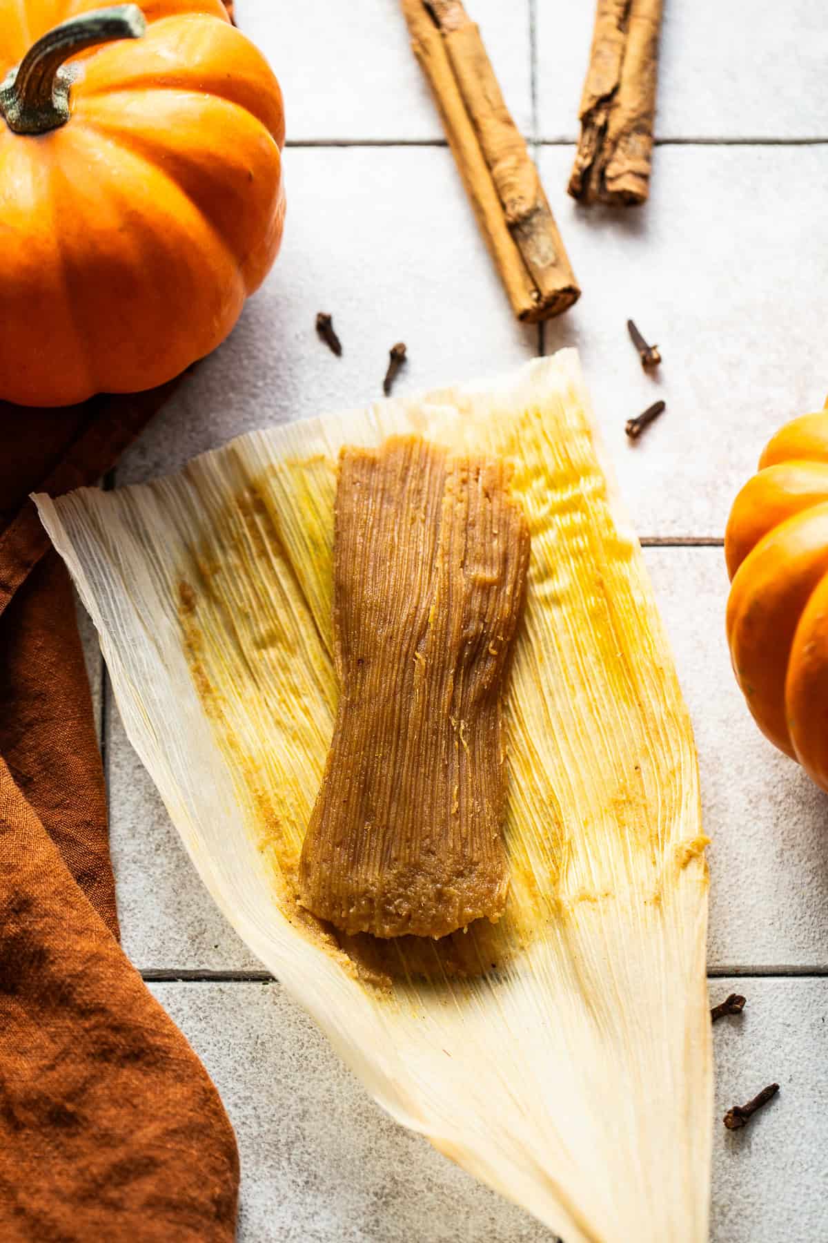 A cooked pumpkin tamal unwrapped and laying on a corn husk.