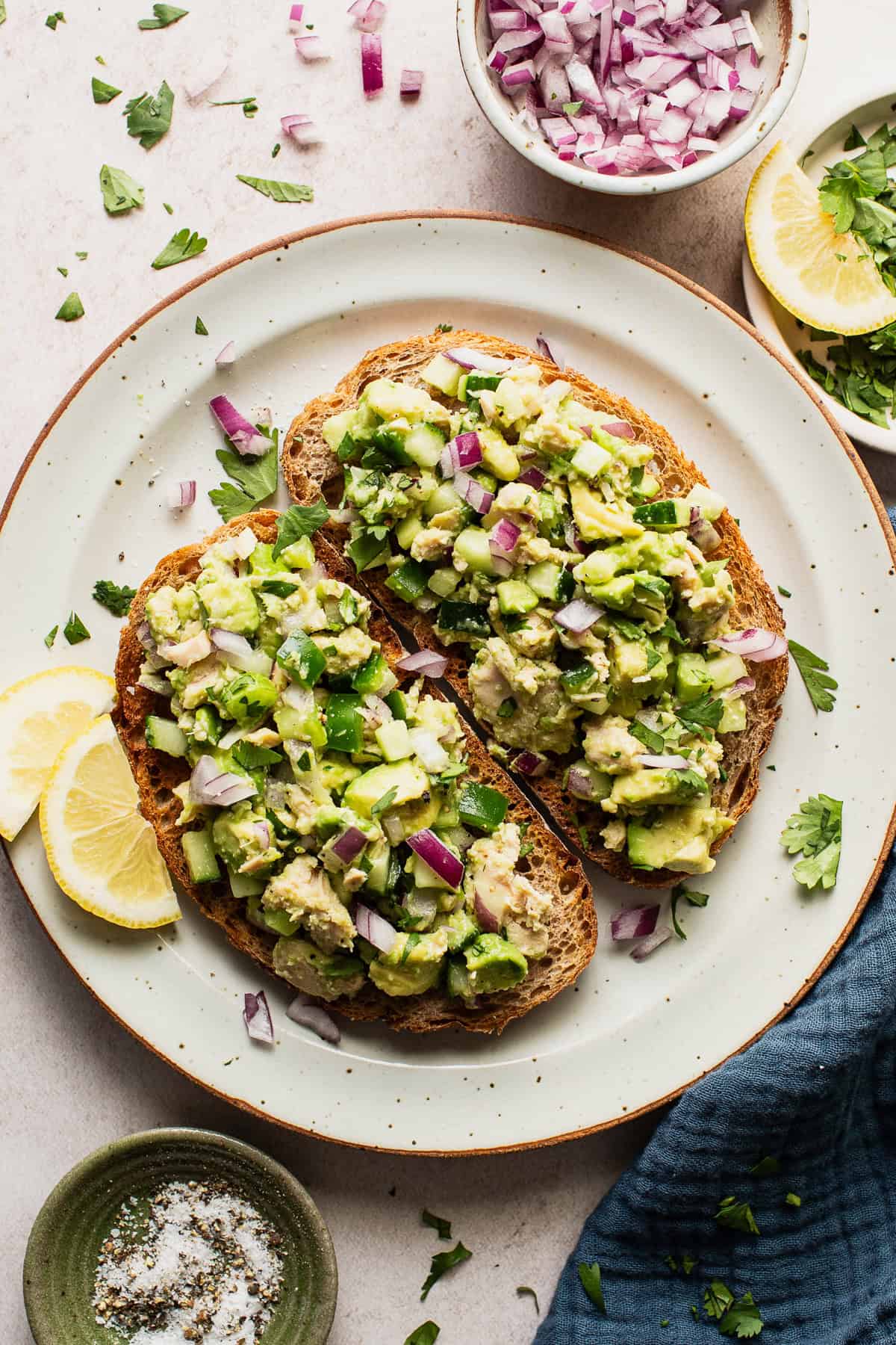 Avocado tuna salad served on toast with a side of lemon slices. 