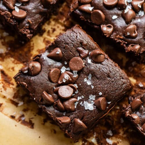 Black bean brownies cut into squares on parchment paper topped with flaky sea salt.