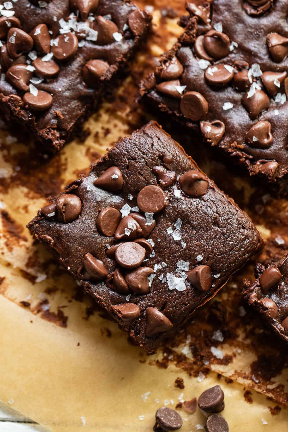 Black bean brownies cut into squares on parchment paper topped with flaky sea salt.