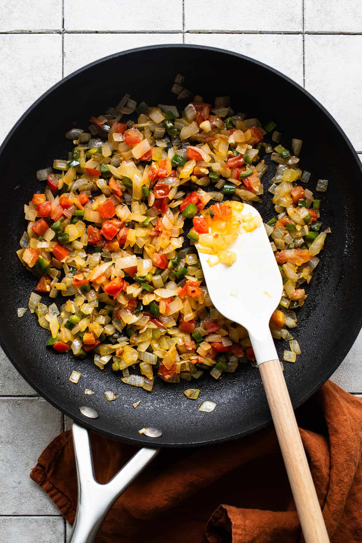 Skillet with all vegetables and peppers in some olive oil being sauteed until tender. 