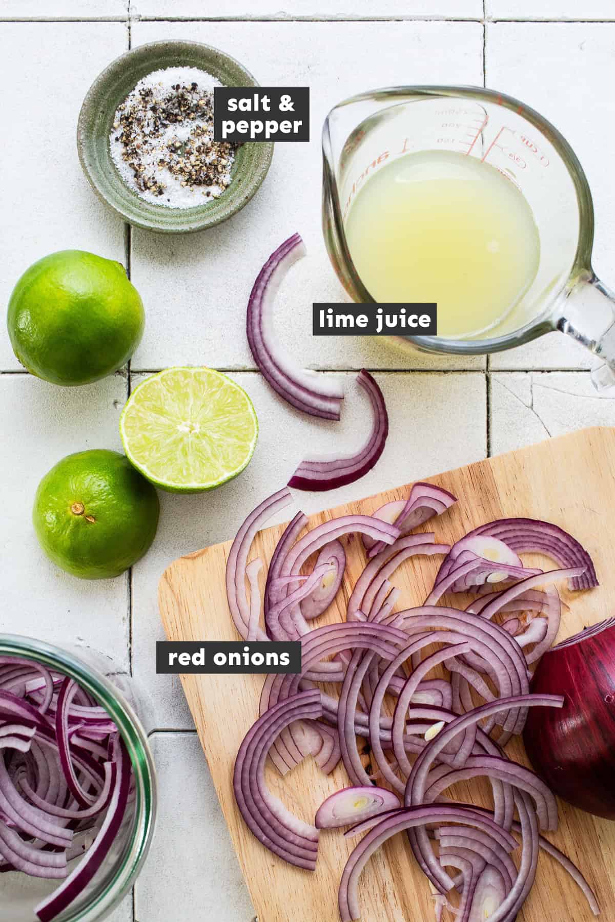 Ingredients in Mexican Pickled Onions on a table - includes salt and black pepper, lime juice, and thinly sliced red onions.