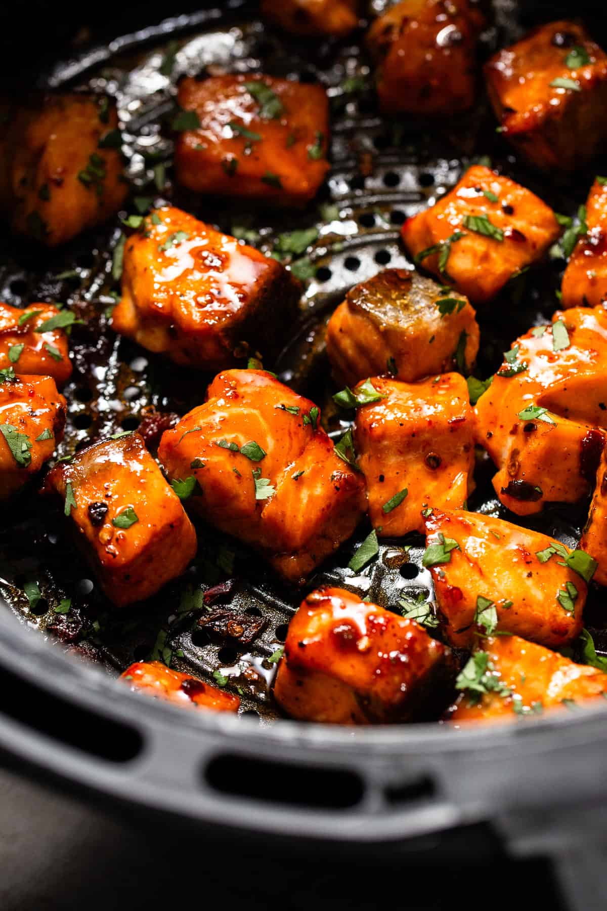 Air fryer salmon bites in an air fryer basket tossed in a chipotle honey sauce.