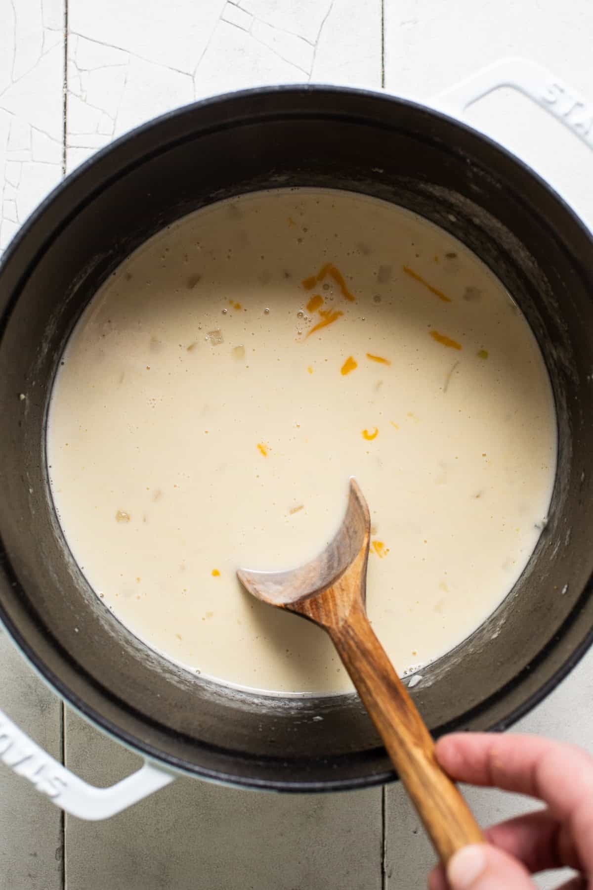 A small pot with broth, heavy cream, and cheese being stirred.