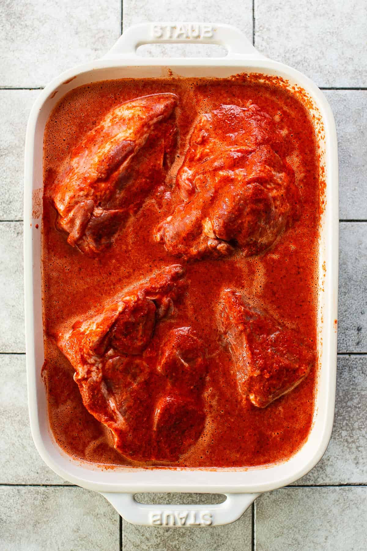 Large chunks of pork shoulder in a bowl covered with cochinita pibil marinade.