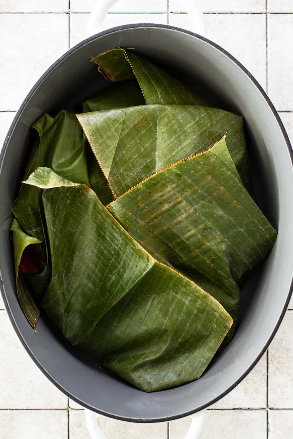 Cochinita pibil wrapped in banana leaves in a large Dutch oven before being braised.