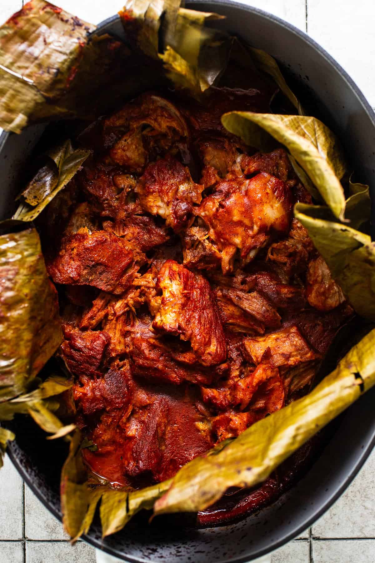 Cochinita pibil slow roasted in a large pot with banana leaves ready to be shredded and served.