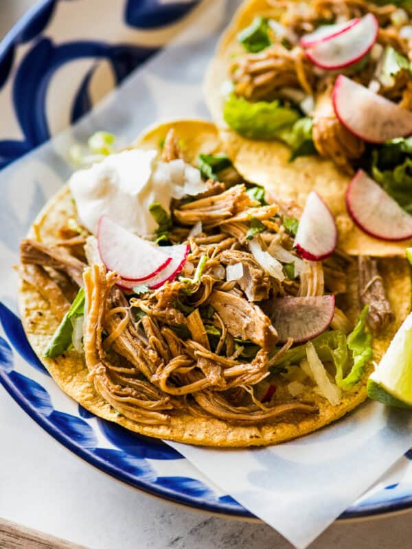 Instant pot chicken tacos served on a dinner plate topped with radishes and limes.