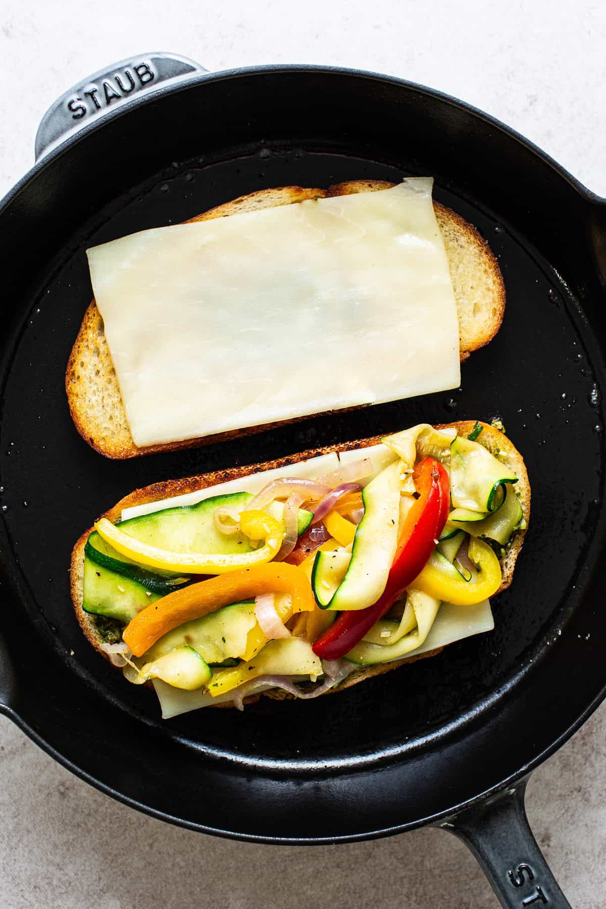 Two slices of bread on a skillet with cheese and the vegetables.