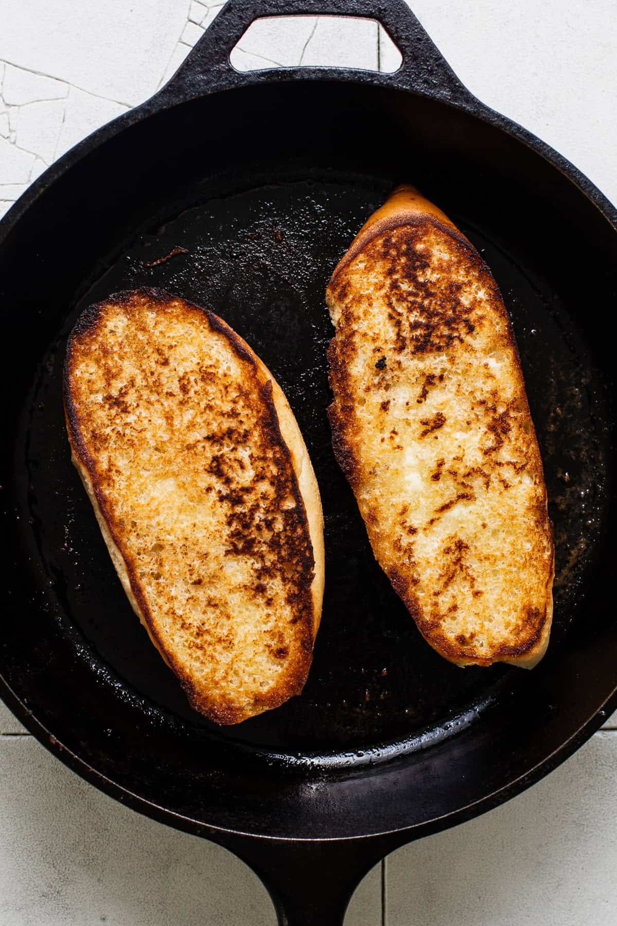 Two slices of bolio bread toasting on a hot skillet.