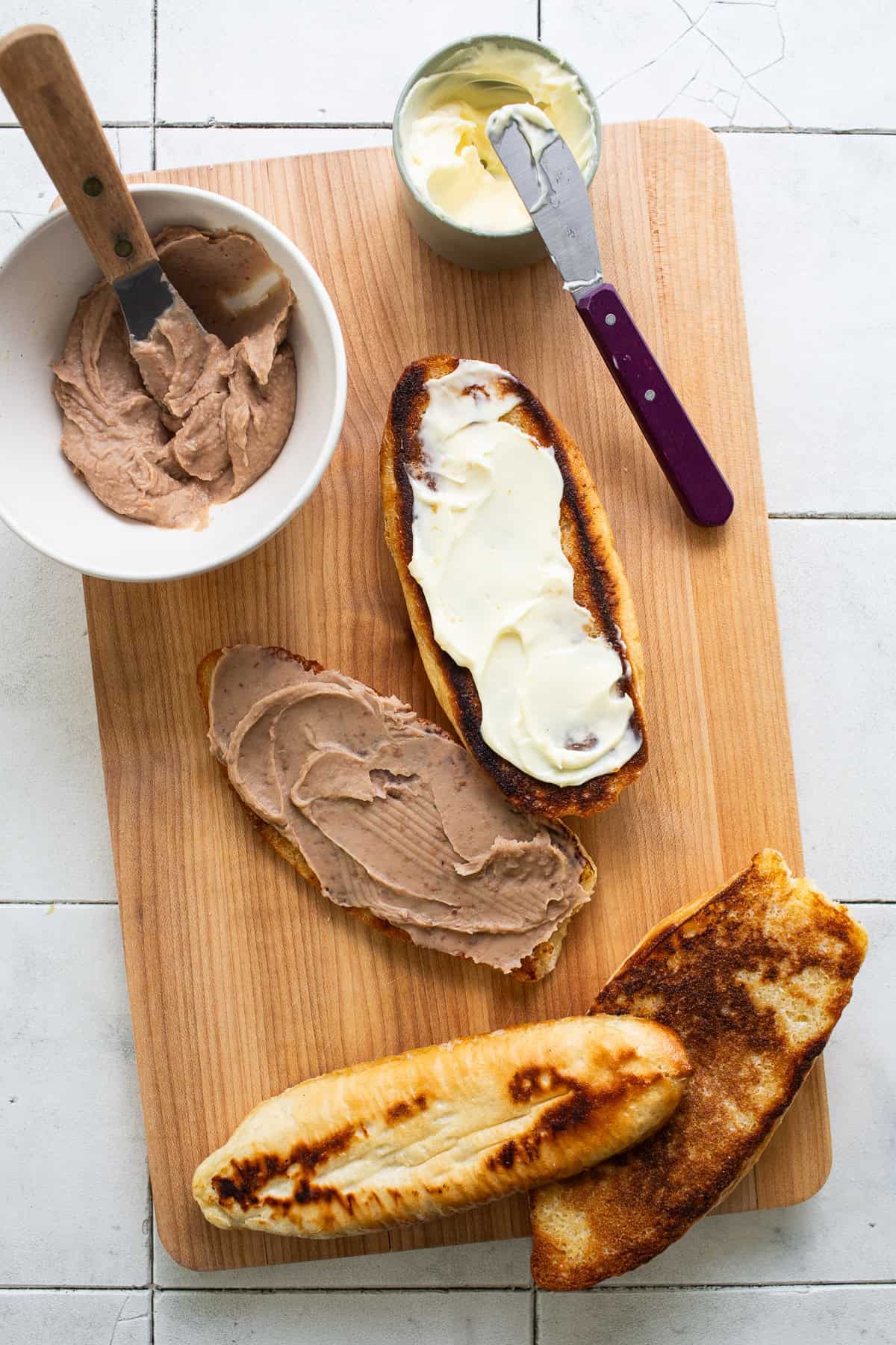 On a cutting board place the toasted bread and begin spreading the beans on the bottom half.