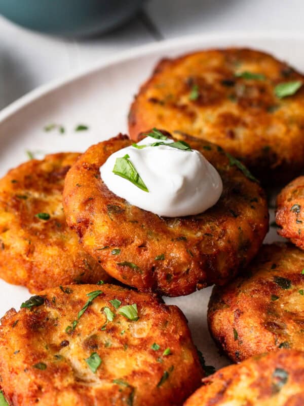 Tortitas de papa freshly made and stacked on a dinner plate with a dollop of sour cream.