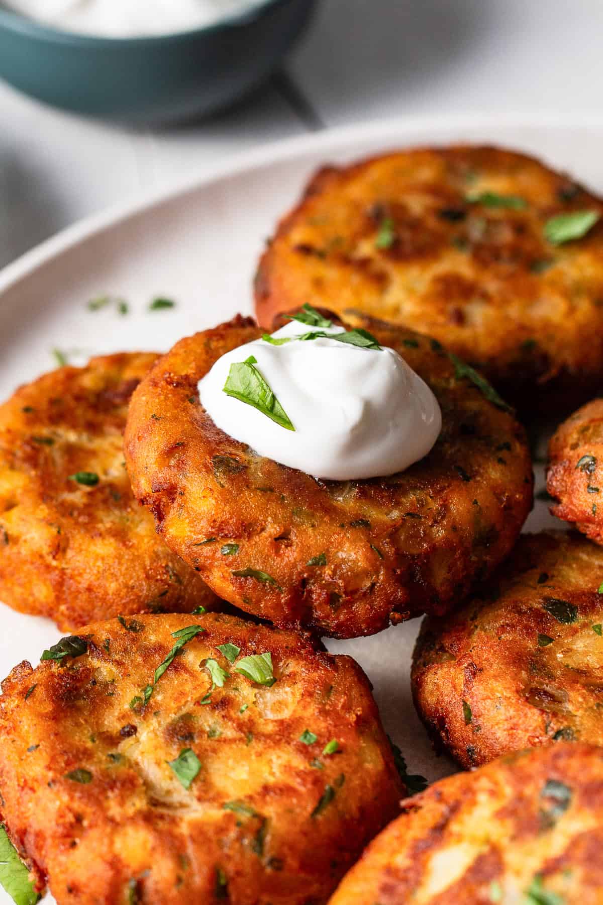 Tortitas de papa freshly made and stacked on a dinner plate with a dollop of sour cream.