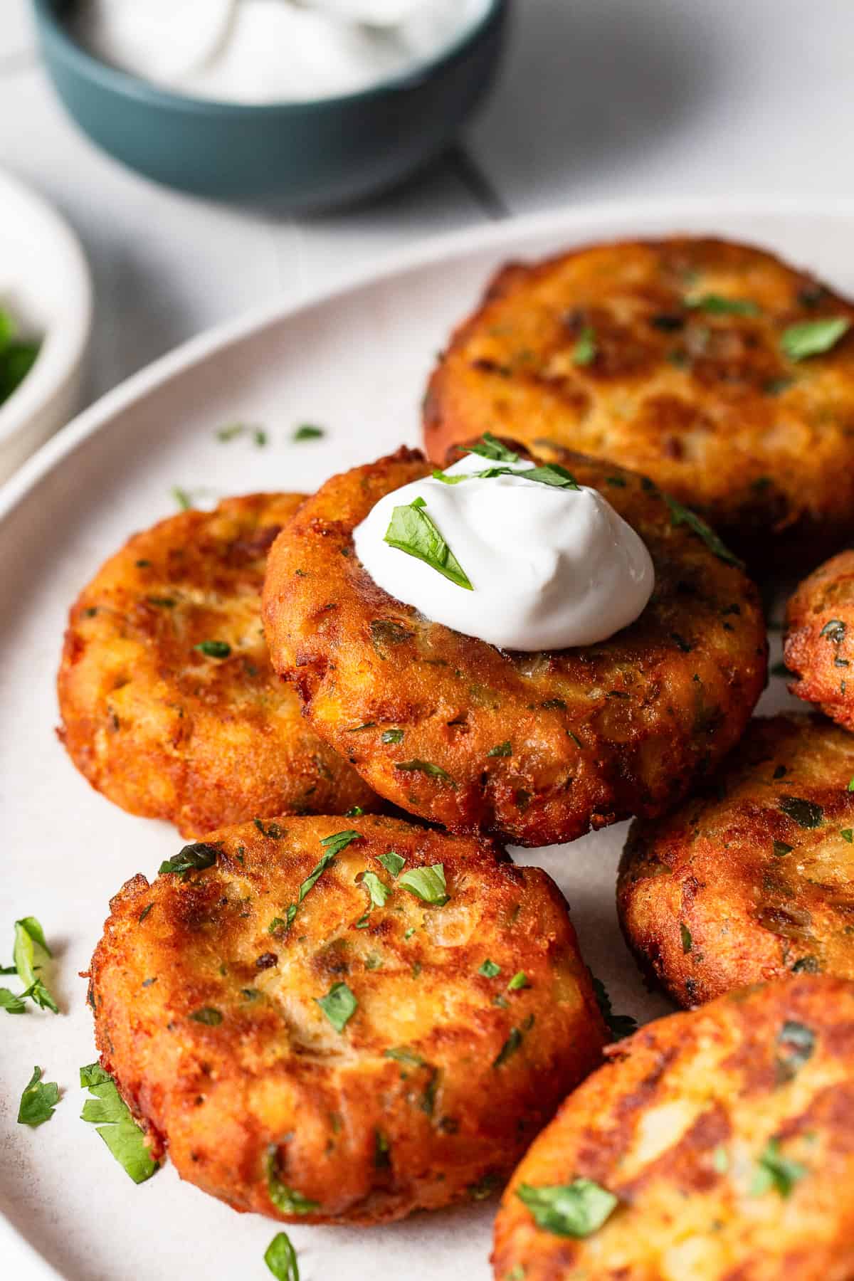 Tortitas de papa freshly made and stacked on a dinner plate with a dollop of sour cream.