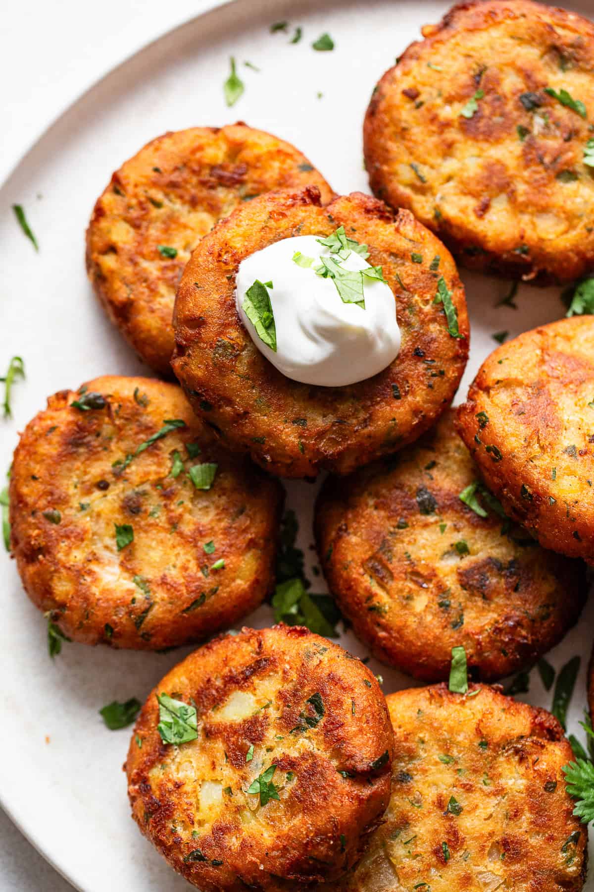 Tortitas de papa stacked on a plate served with a dollop of sour cream.